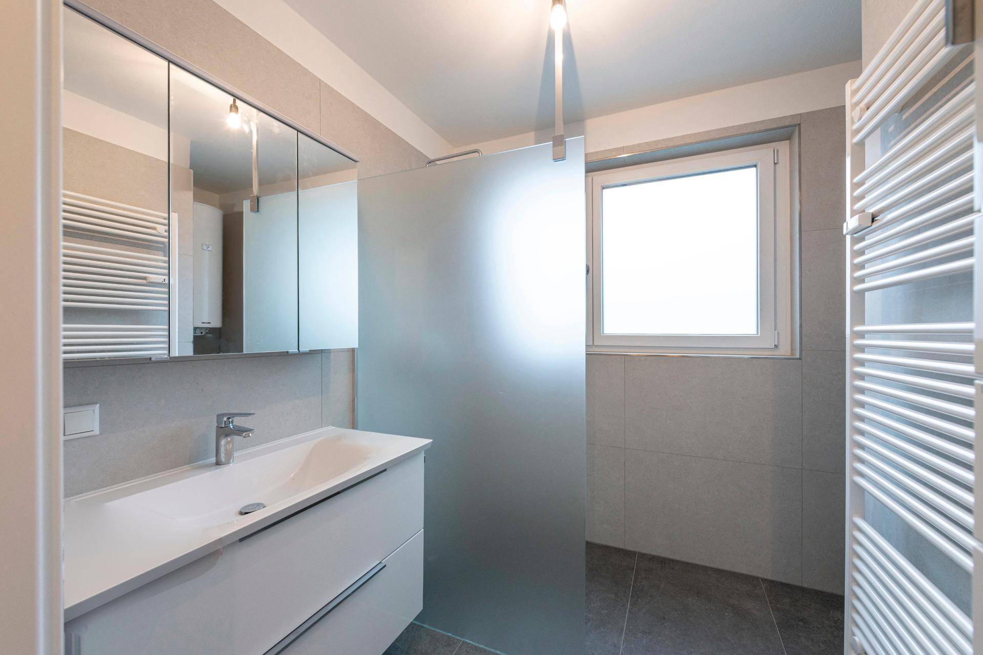 Modernes Badezimmer mit Dusche, Waschtisch und beheiztem Handtuchhalter.