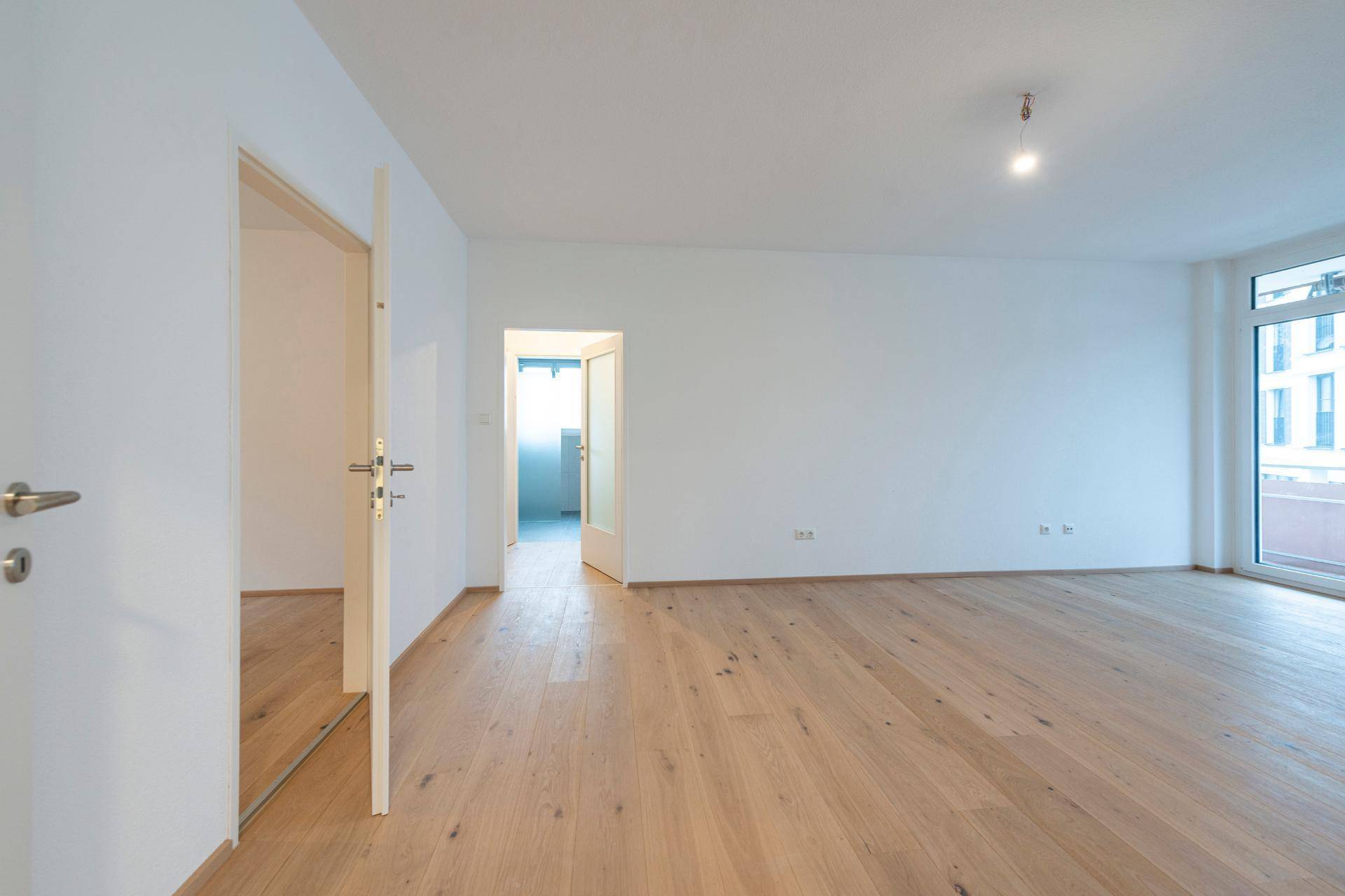 Geräumiges Wohnzimmer mit hellem Parkettboden und Blick auf die Umgebung.