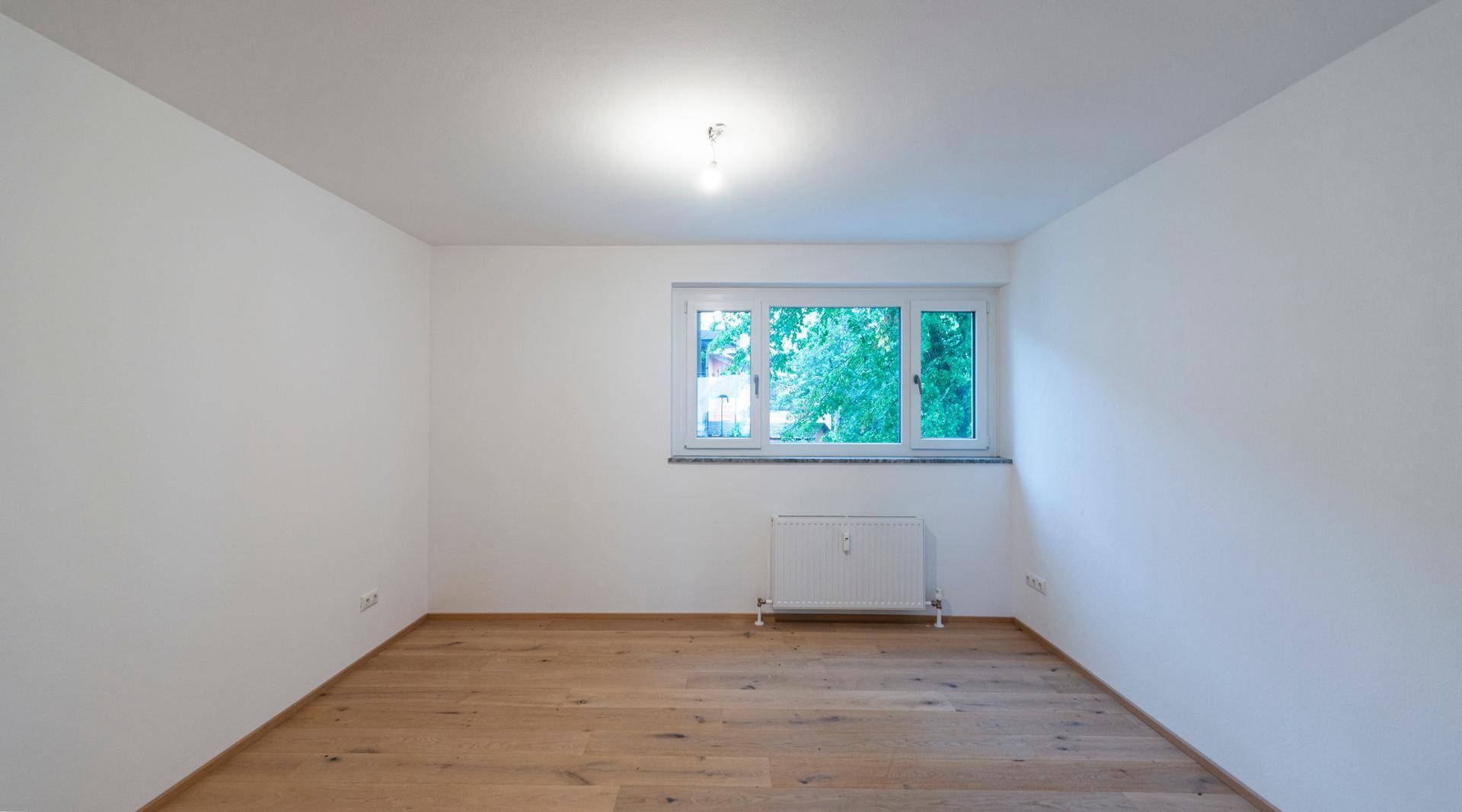 Schlafzimmer mit hellem Parkettboden und Fenster mit Blick ins Grüne.
