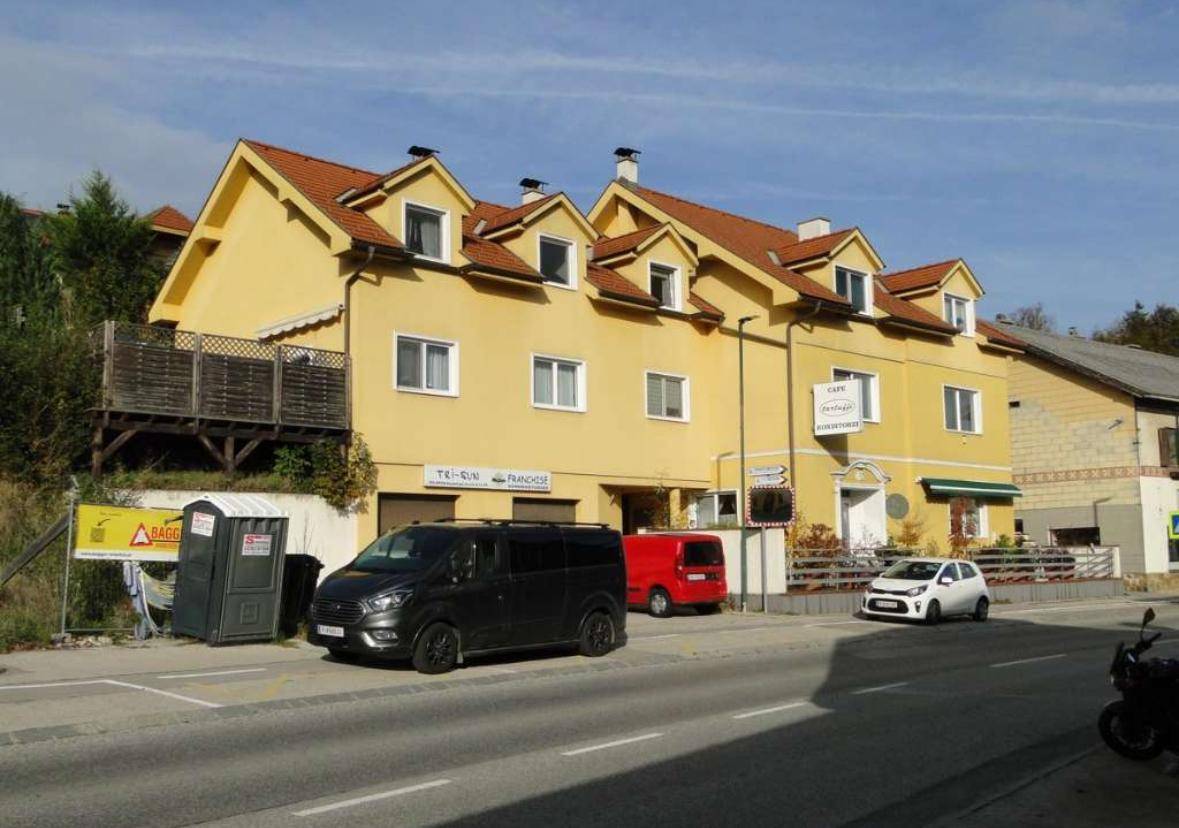 Gelbes Gebäude mit rotem Dach und mehreren Gaubenfenstern an einer Straße gelegen.