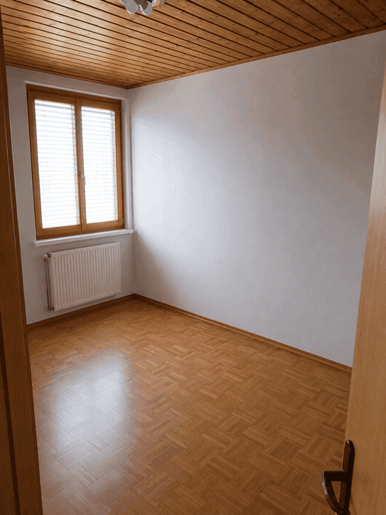 Helles Zimmer mit Holzdecke und Parkettboden, ausgestattet mit einem Fenster und Heizkörper.
