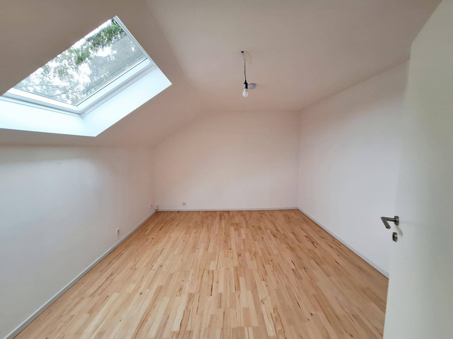 Helles Zimmer im Dachgeschoss mit Holzboden und großem Dachfenster, ideal als Schlafzimmer.