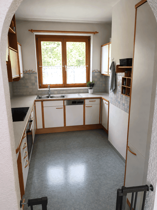 Funktionale Küche mit U-förmiger Arbeitsplatte, Einbaugeräten und Fenster, gut beleuchtet.