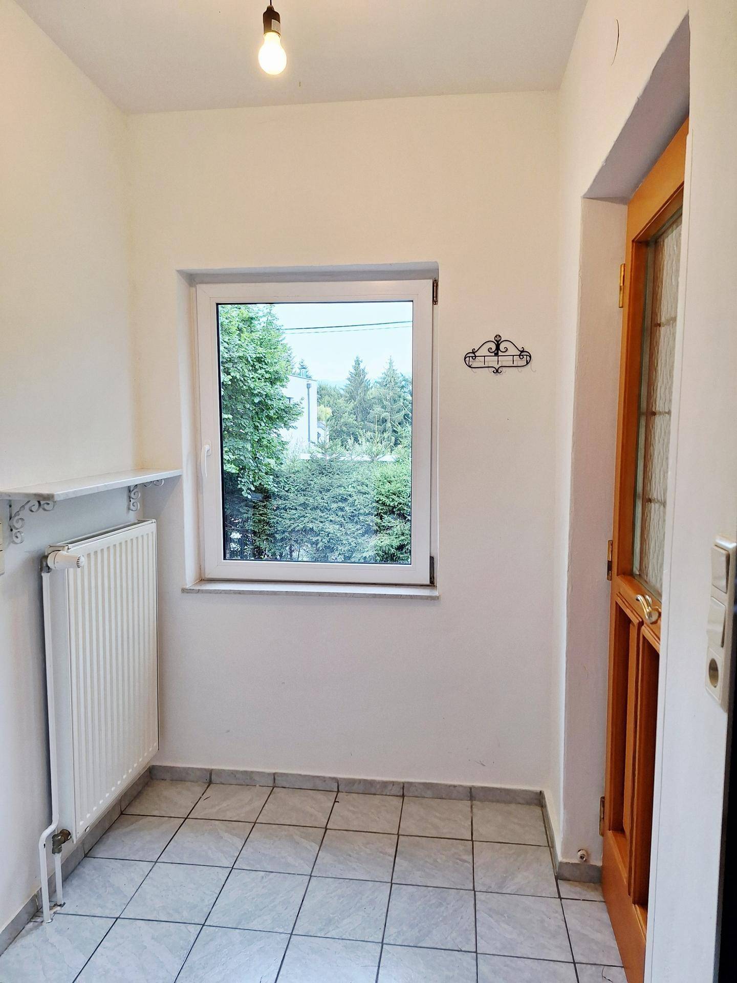 Eingangsbereich mit Fliesenboden, Fenster und Garderobenhaken, hell und funktional.