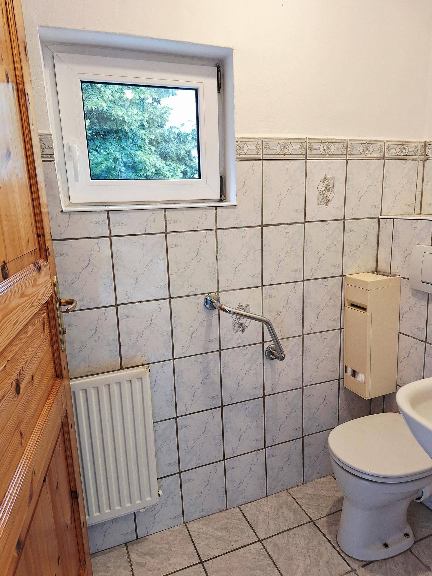 Kleines Gäste-WC mit hellen Fliesen, Fenster und Haltegriff für zusätzliche Sicherheit.