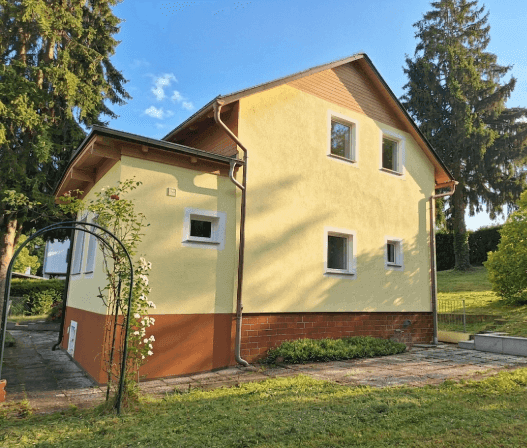 Seitenansicht des Hauses mit Gartenbereich und gepflegter Rasenfläche unter blauem Himmel.