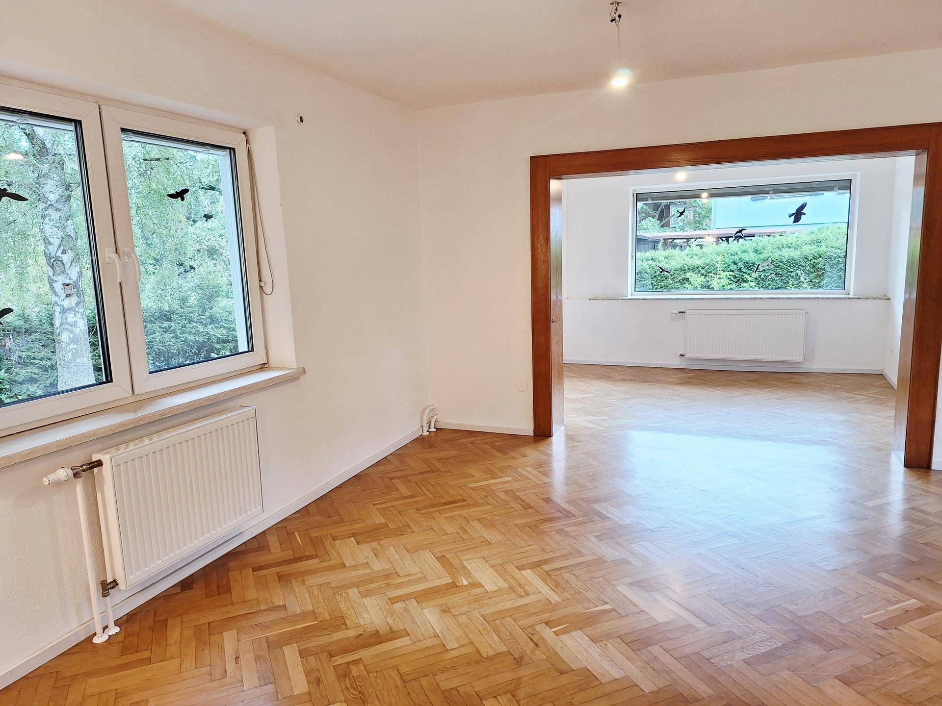 Helles Wohnzimmer mit Fischgrätparkett und Blick ins Grüne durch große Fenster.