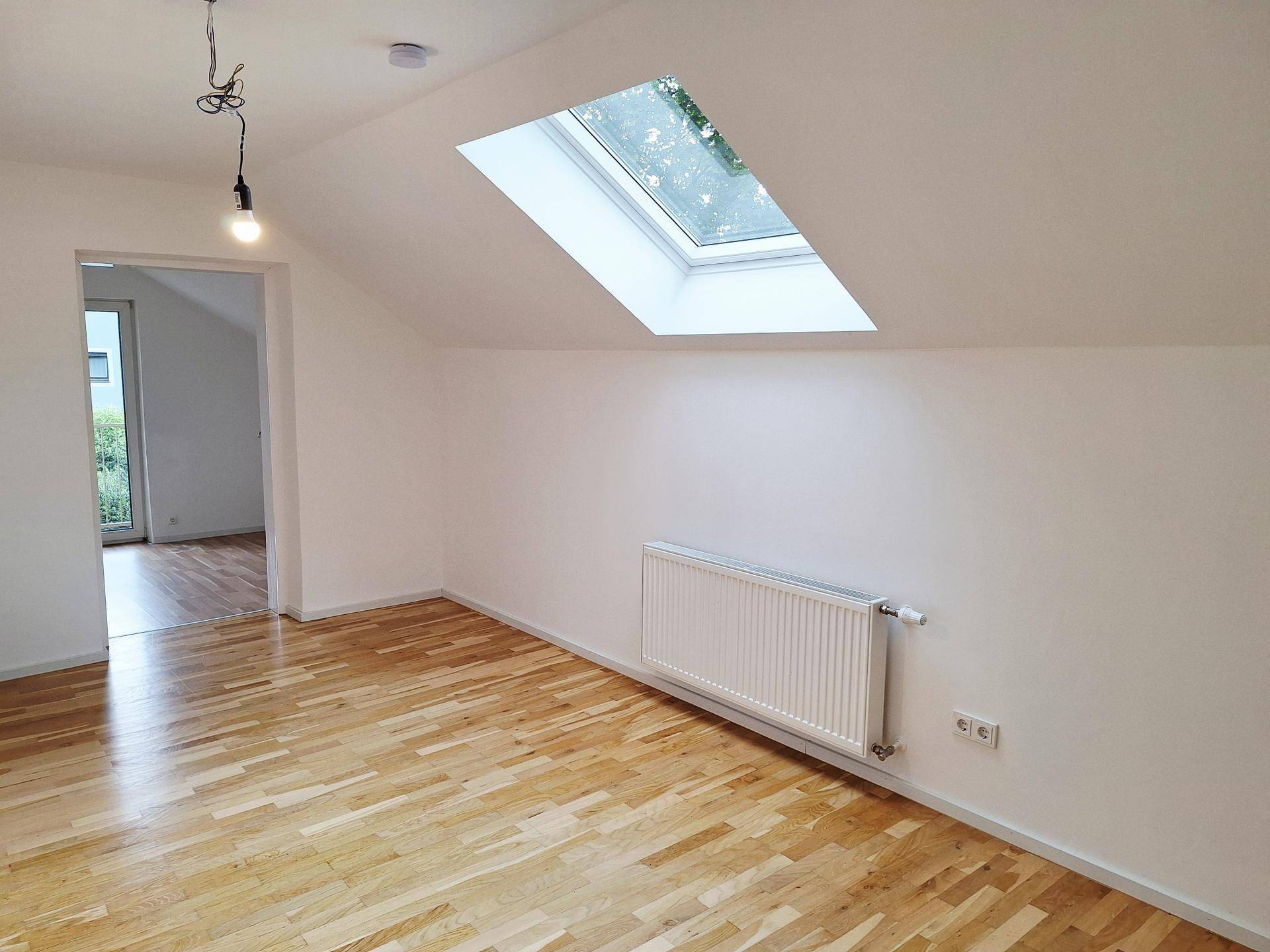 Dachgeschosszimmer mit Holzboden, Heizkörper und Dachfenster, bietet viel Tageslicht.