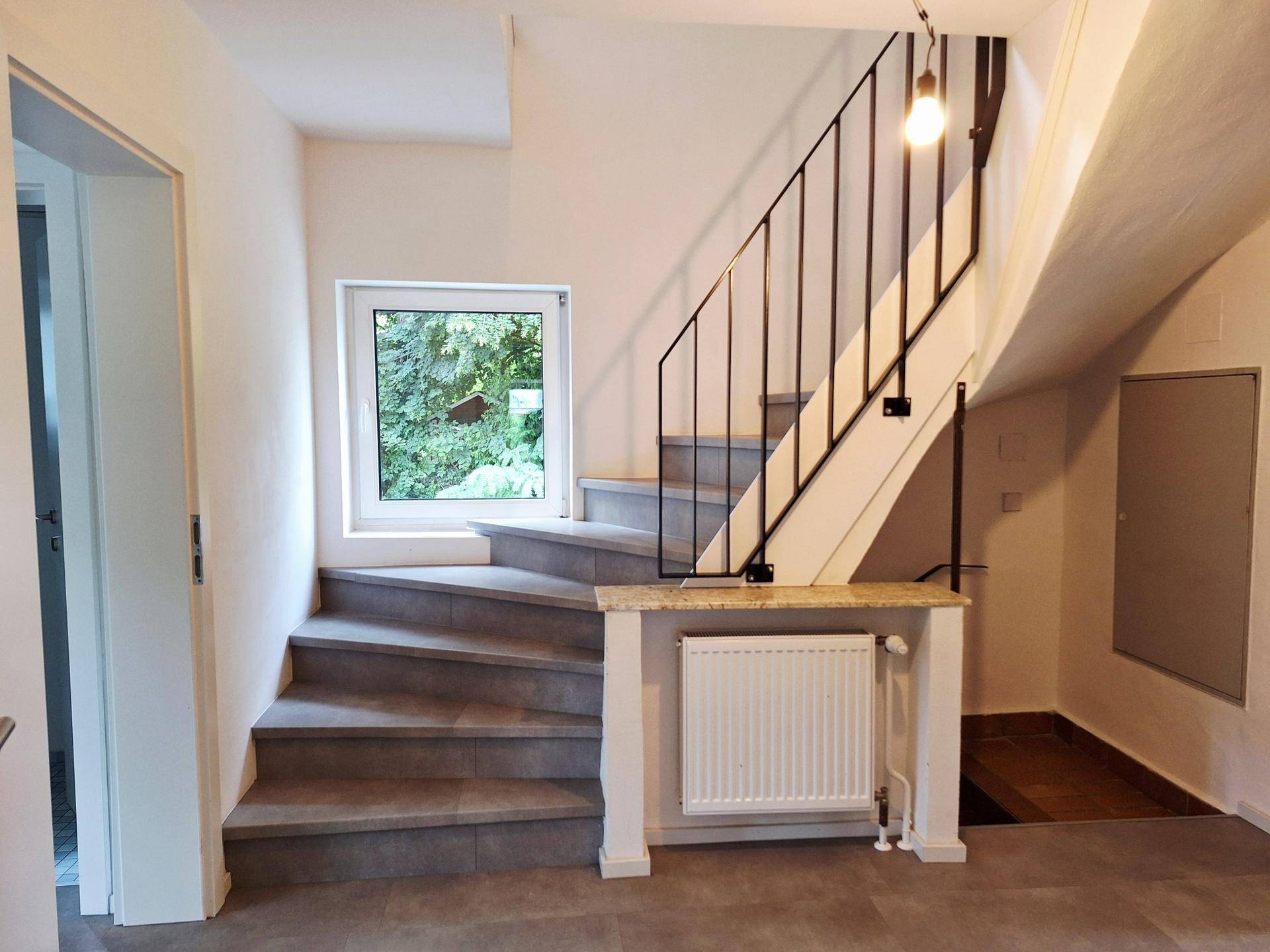 Heller Treppenaufgang mit Fliesenstufen und modernem Geländer, führt in die obere Etage.