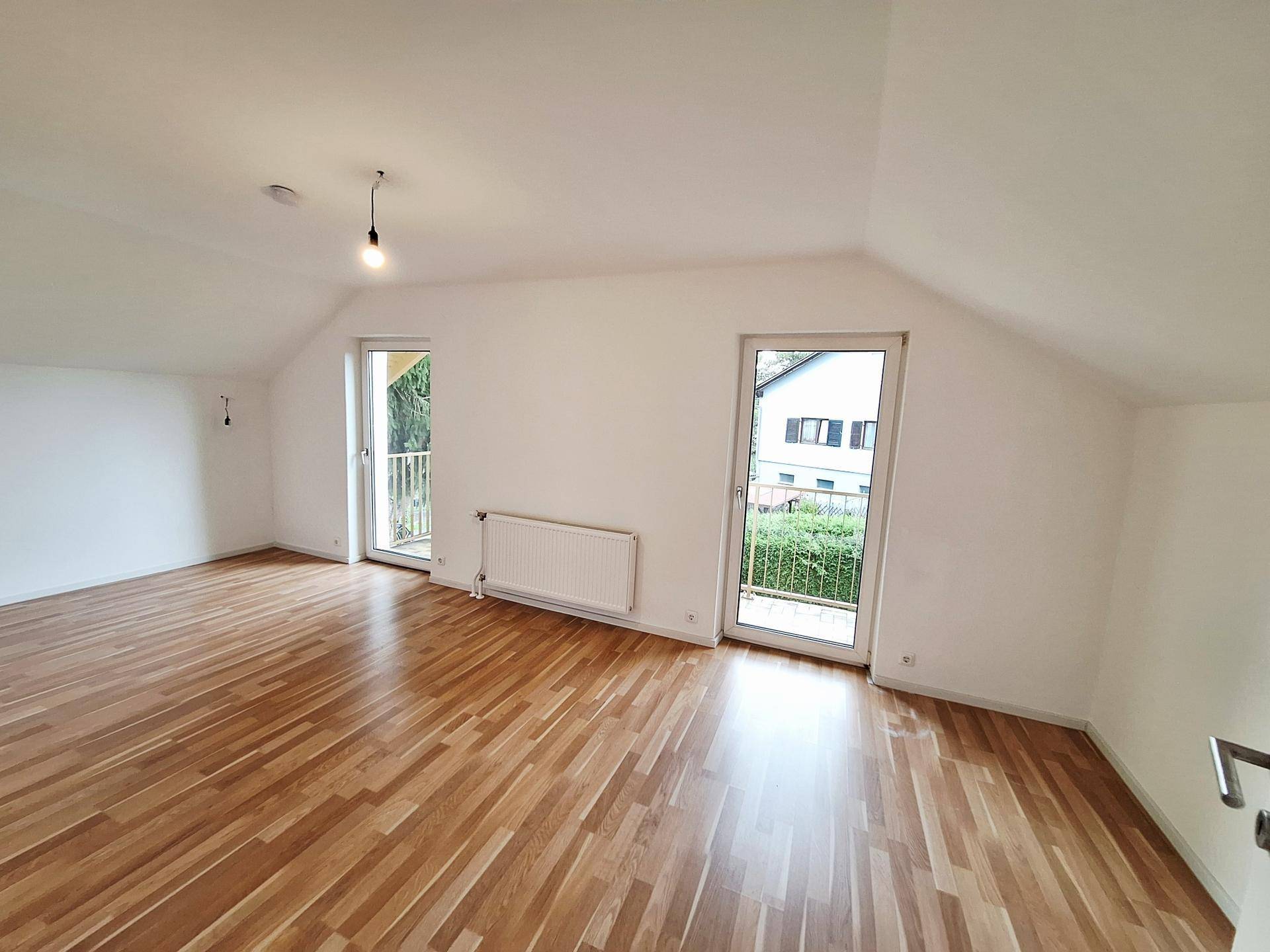 Geräumiges Zimmer mit Holzboden und Zugang zu einem französischen Balkon, hell und luftig.