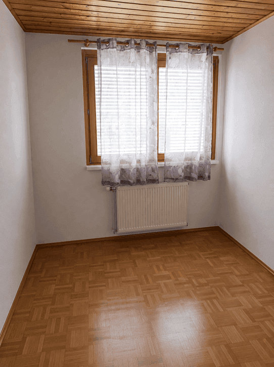 Helles Zimmer mit Holzdecke und Parkettboden, ausgestattet mit Fenster und Vorhängen.