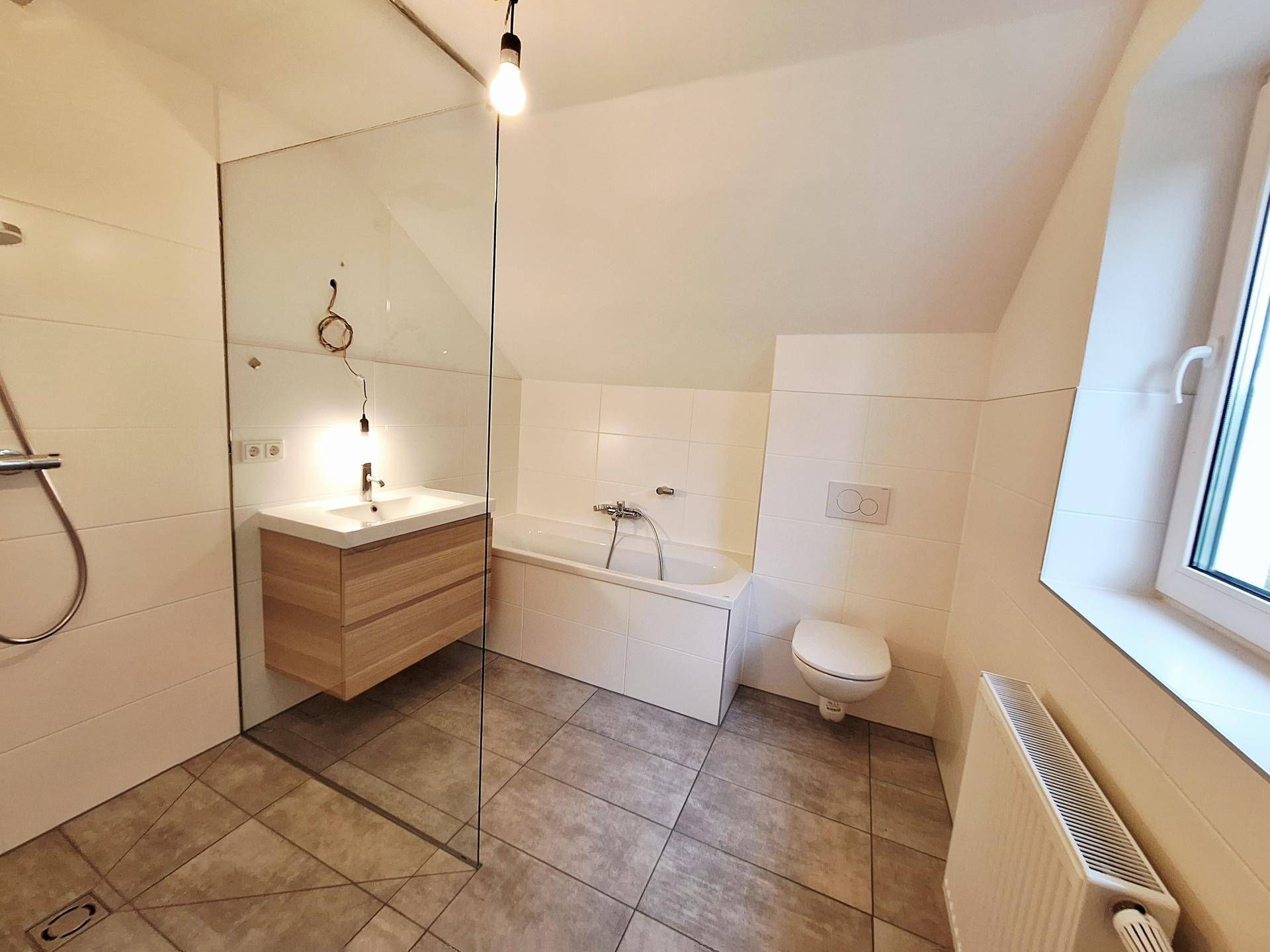Modernes Badezimmer mit Badewanne, begehbarer Dusche und Dachschräge, hell gefliest.
