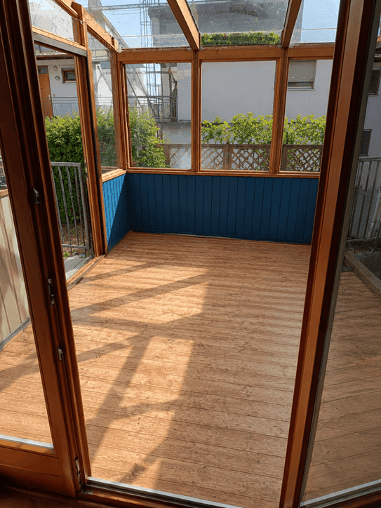 Heller Wintergarten mit Holzfußboden und blauer Wandverkleidung, ideal für entspannte Stunden.