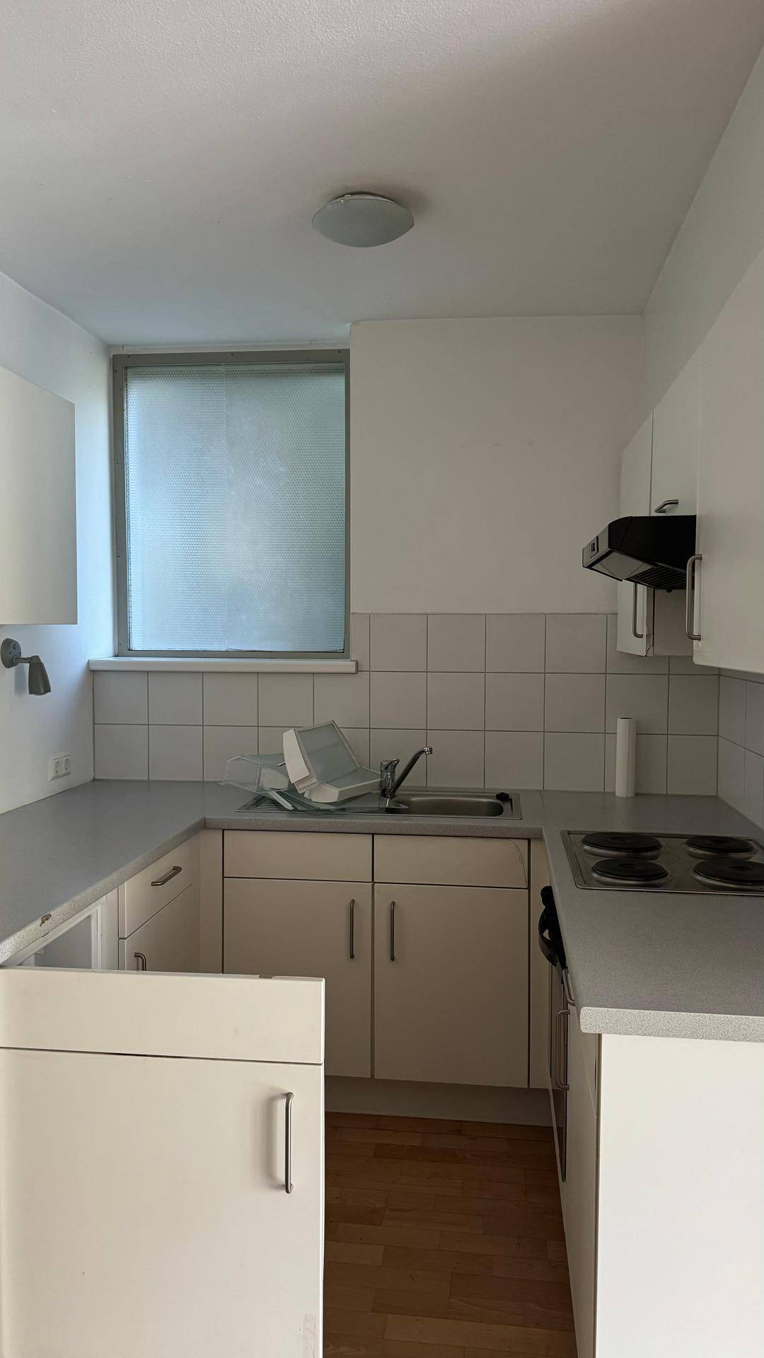 Helle Küche mit weißen Schränken, Kochfeld, Kühlschrank und Fenster.