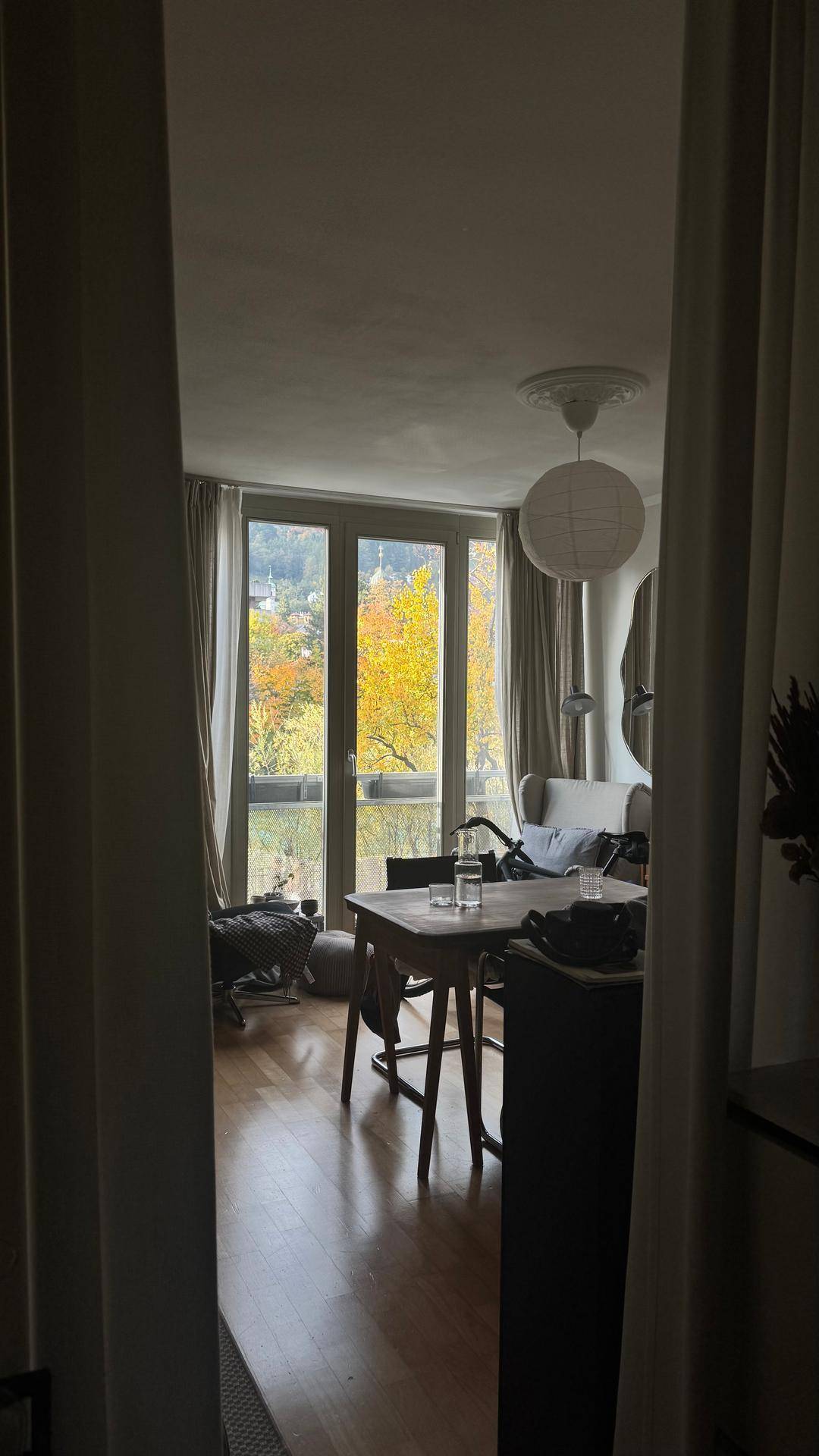 Blick in einen Wohnbereich mit Esstisch und großen Fenstern mit Herbstlaubblick.