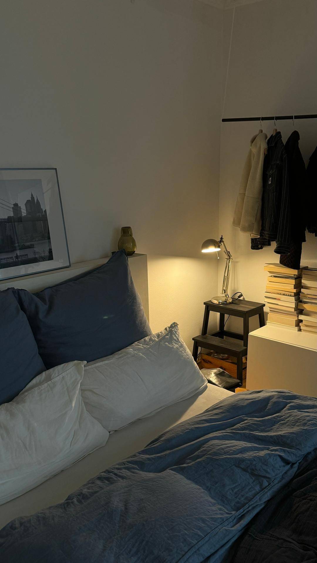 Gemütliches Schlafzimmer mit Bett, Nachttischlampe und Kleiderstange.