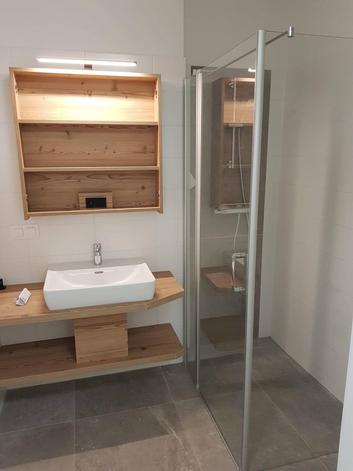 Helles, modernes Badezimmer mit Holzwaschtisch, Aufsatzwaschbecken und geräumiger Glasdusche.