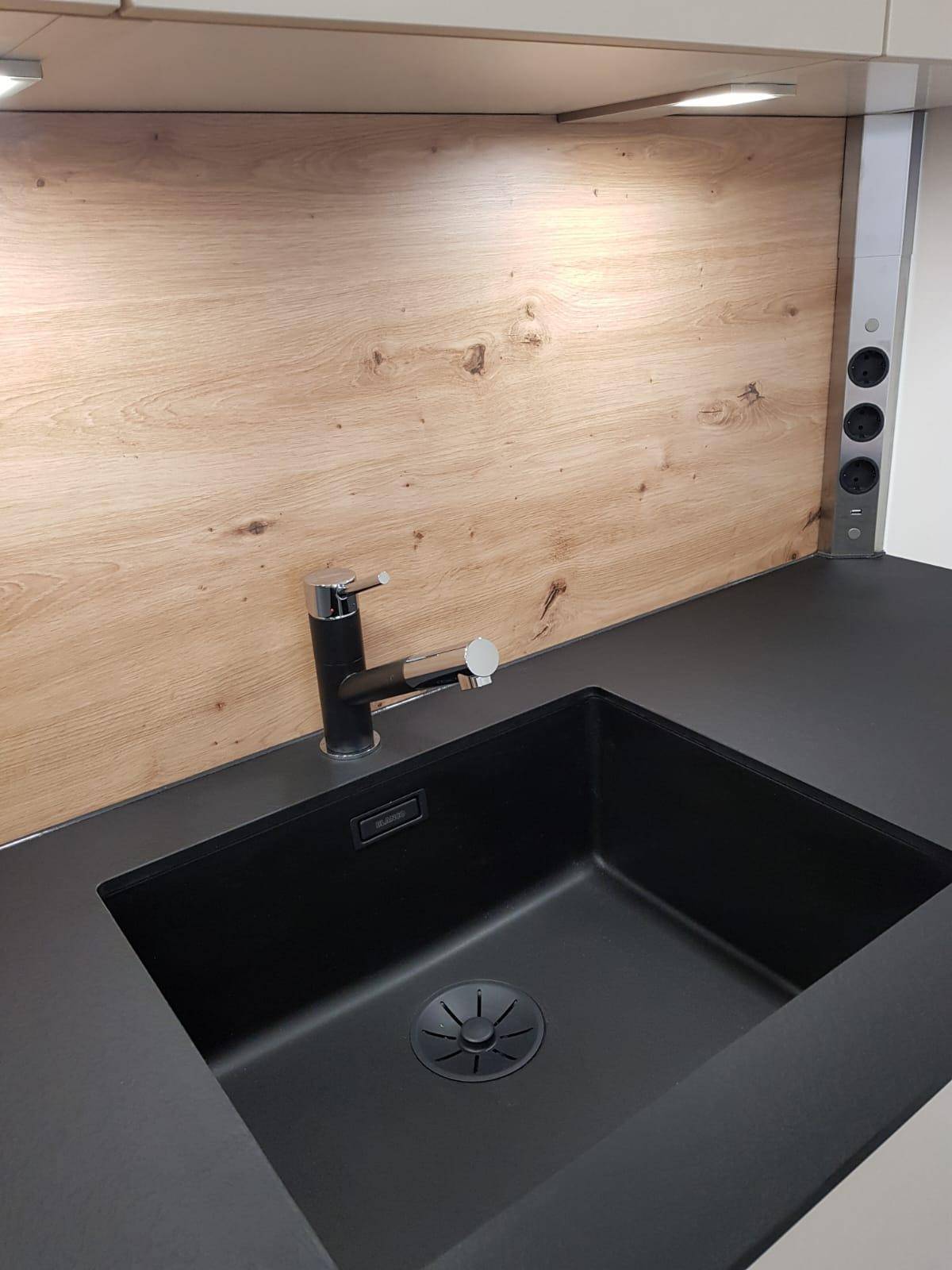 Detailaufnahme des modernen schwarzen Spülbeckens mit Armatur und Holzrückwand in der Küche.