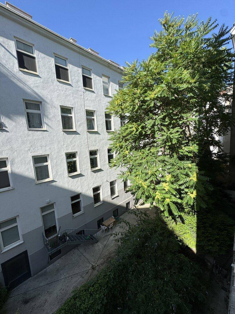Innenhof eines Wohngebäudes mit Bäumen und hellblauer Fassade.