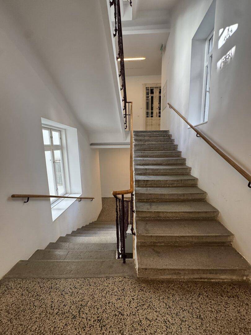 Historisches Treppenhaus mit Steinstufen, Holzgeländer und Terrazzoboden.