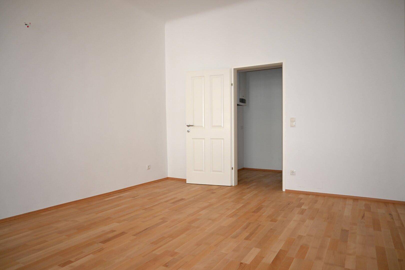 Leeres Zimmer mit Parkettboden und weißer Tür, bietet vielseitige Nutzungsmöglichkeiten.