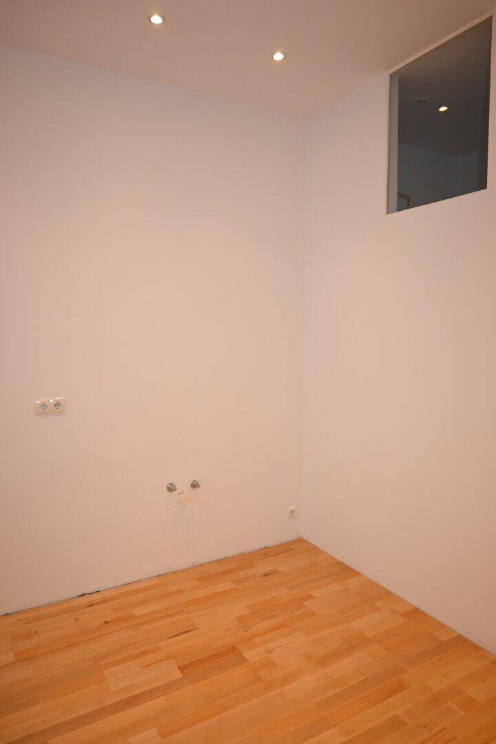 Ecke eines Raumes mit Anschlüssen und einem kleinen Fenster, möglicherweise für eine Küche.