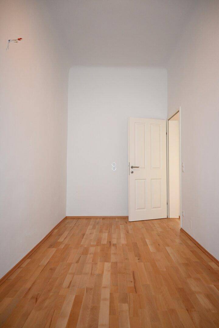 Schmaler Raum mit Parkettboden und weißer Tür, ideal für ein Arbeitszimmer oder Gästezimmer.