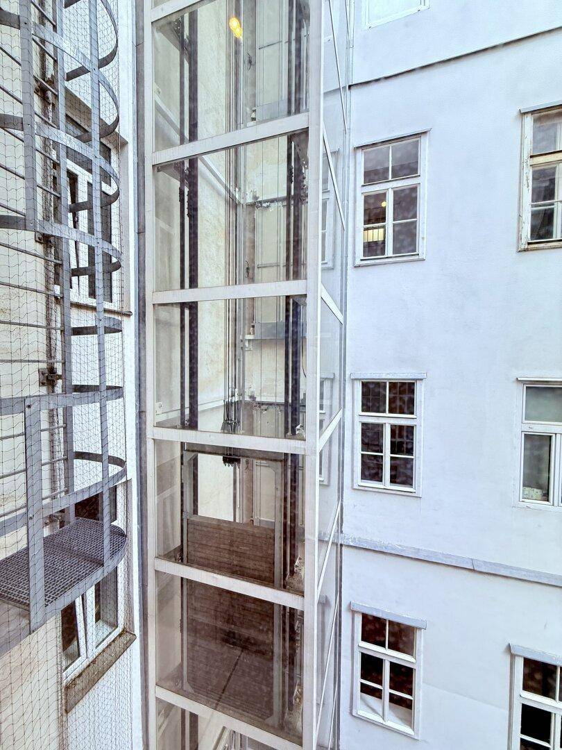 Außenaufzug aus Glas und Metall an der Fassade eines Wohngebäudes.