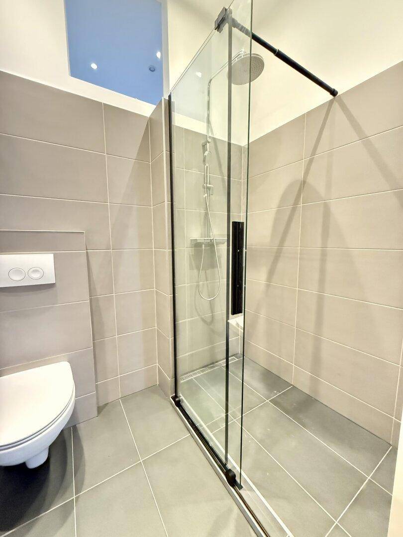 Modernes Badezimmer mit grauen Fliesen, Glasduschwand und ebenerdiger Dusche.