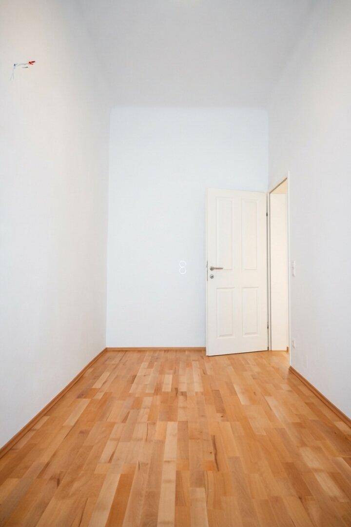 Leeres Zimmer mit hellem Parkettboden und einer weißen Tür, bereit zur individuellen Gestaltung.