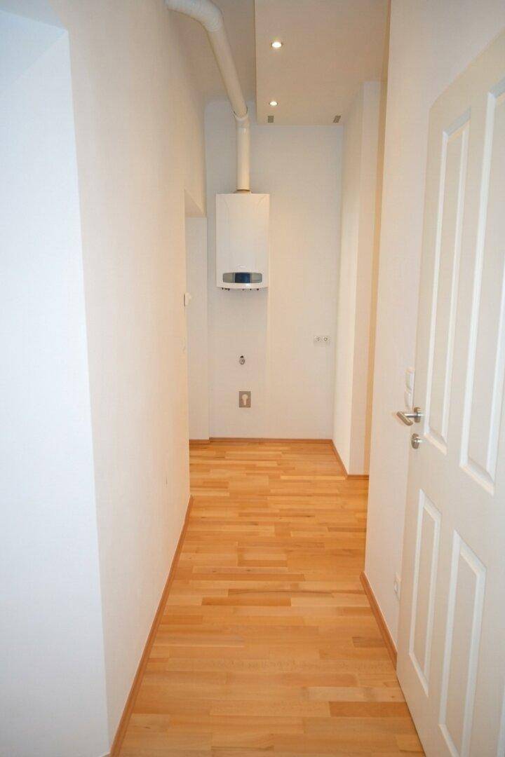 Heller Flur mit Parkettboden, Einbaustrahlern und einem Warmwasserbereiter an der Wand.