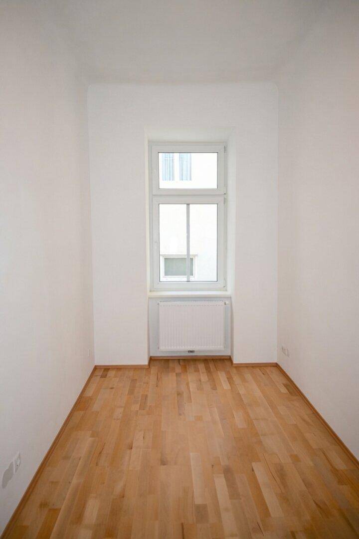 Gemütliches Zimmer mit einem Fenster, Heizkörper und warmem Parkettboden, ideal als Schlafzimmer.