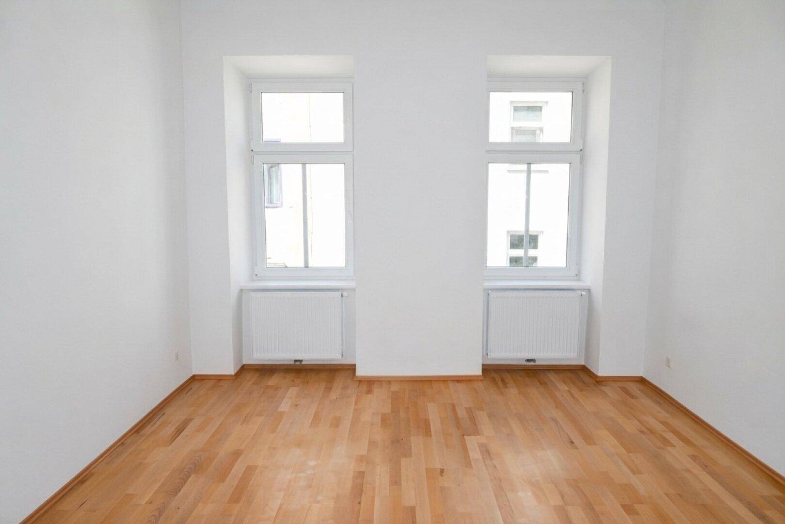 Helles Zimmer mit zwei Fenstern, Heizkörpern und schönem Parkettboden, ideal für Wohnzwecke.