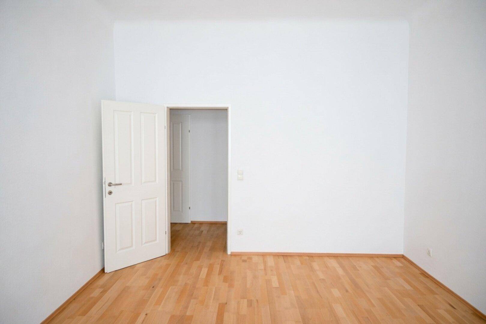 Geräumiges Zimmer mit Holzboden und einer offenen Tür, die zu einem weiteren Raum führt.