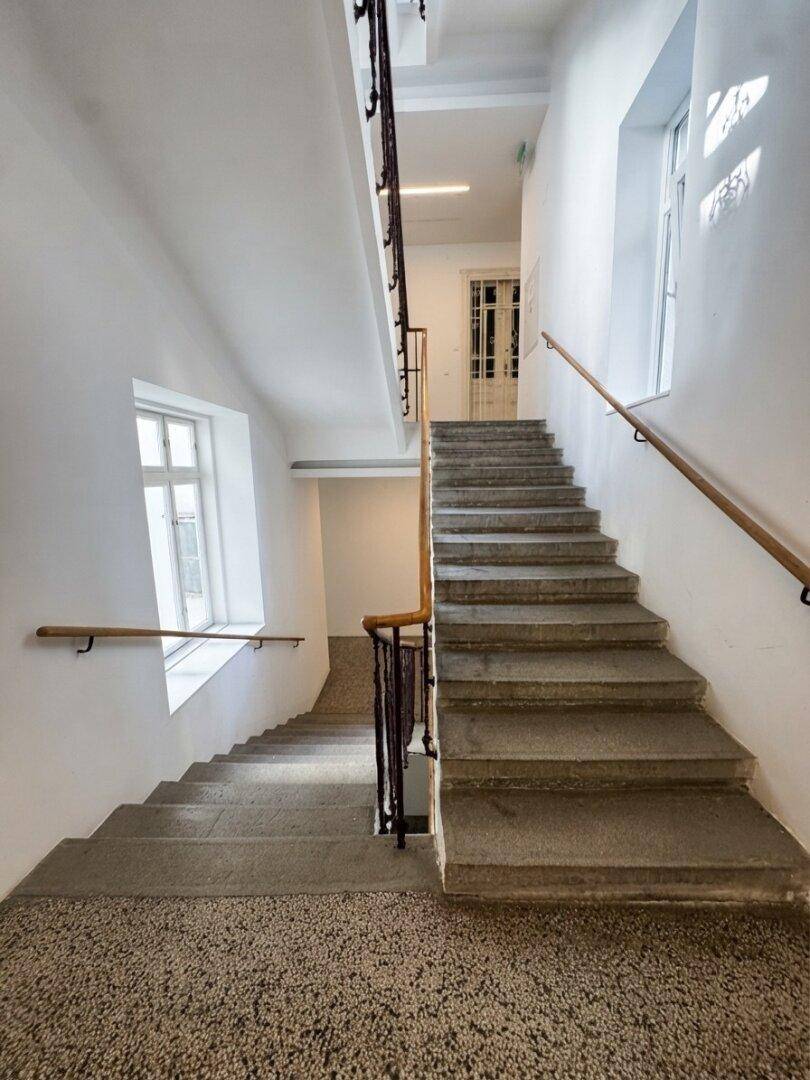 Helles Treppenhaus mit Steinstufen, Holzgeländer und Fenstern für natürliches Licht.