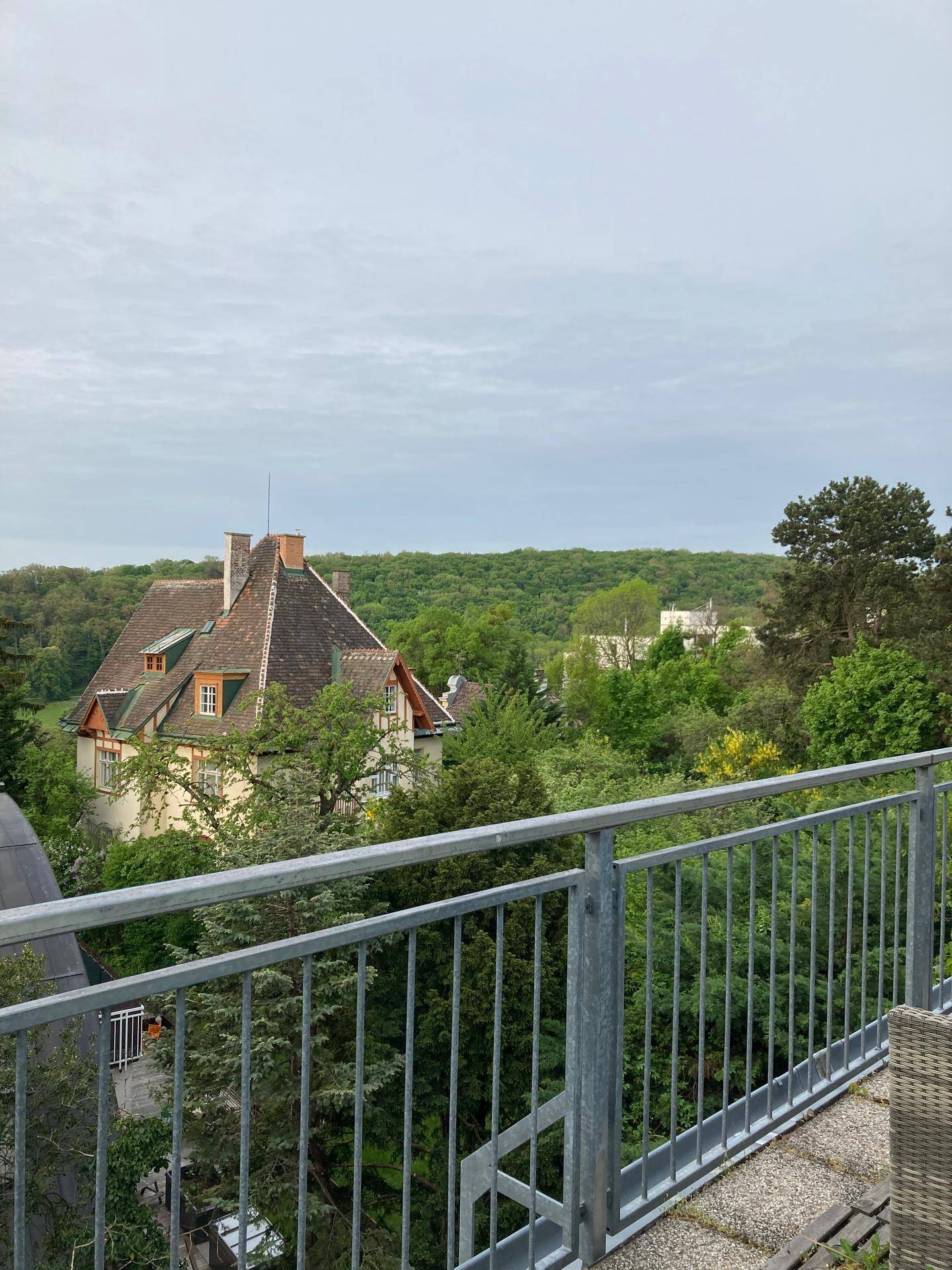 Balkon mit Blick auf ein charmantes Haus mit Mansarddach inmitten üppiger grüner Bäume.