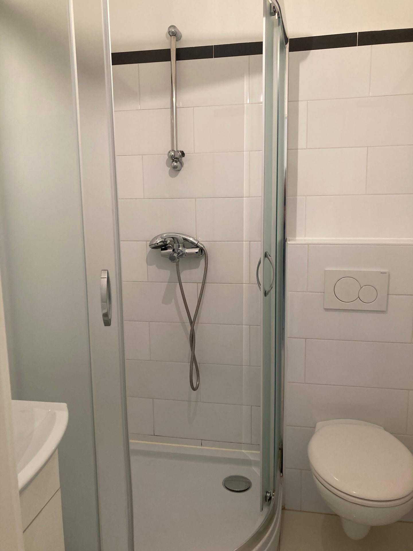 Badezimmer mit Duschkabine und wandhängendem WC, komplett gefliest in Weiß.