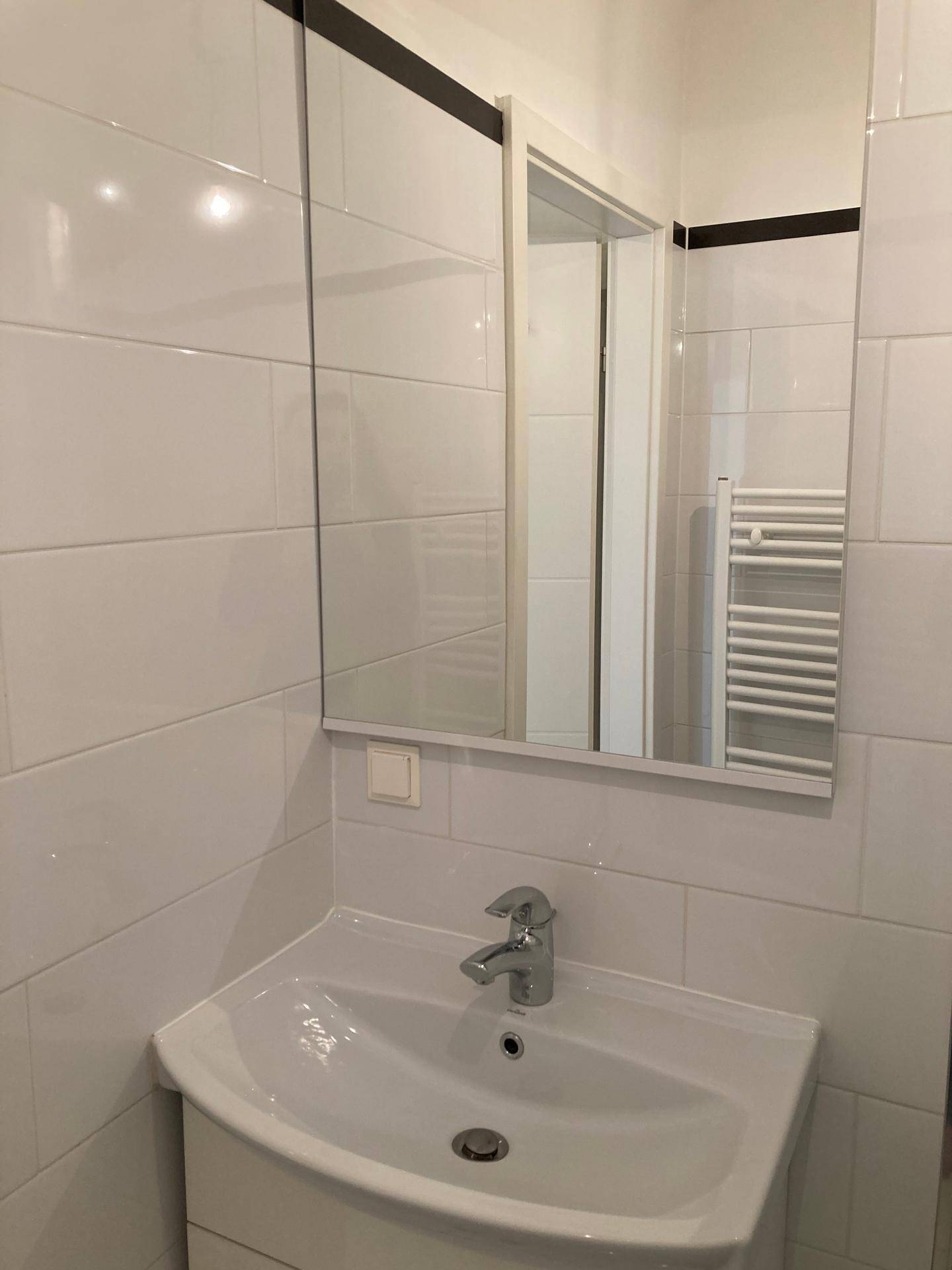 Modernes Badezimmer mit weißem Waschbecken, Spiegel und weißen Wandfliesen.