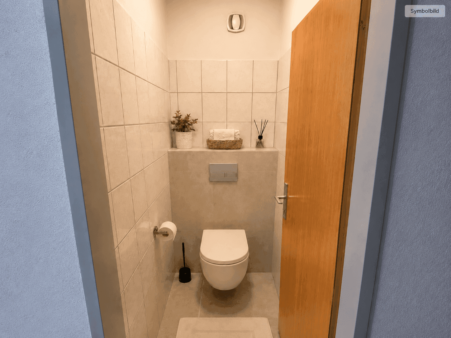 Separates WC mit wandhängender Toilette und hellen Fliesen an Wänden und Boden.