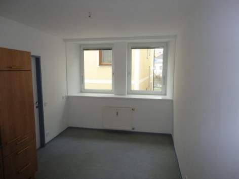 Leerer Raum mit zwei Fenstern, die viel Tageslicht hereinlassen und einen Blick auf die Umgebung bieten.