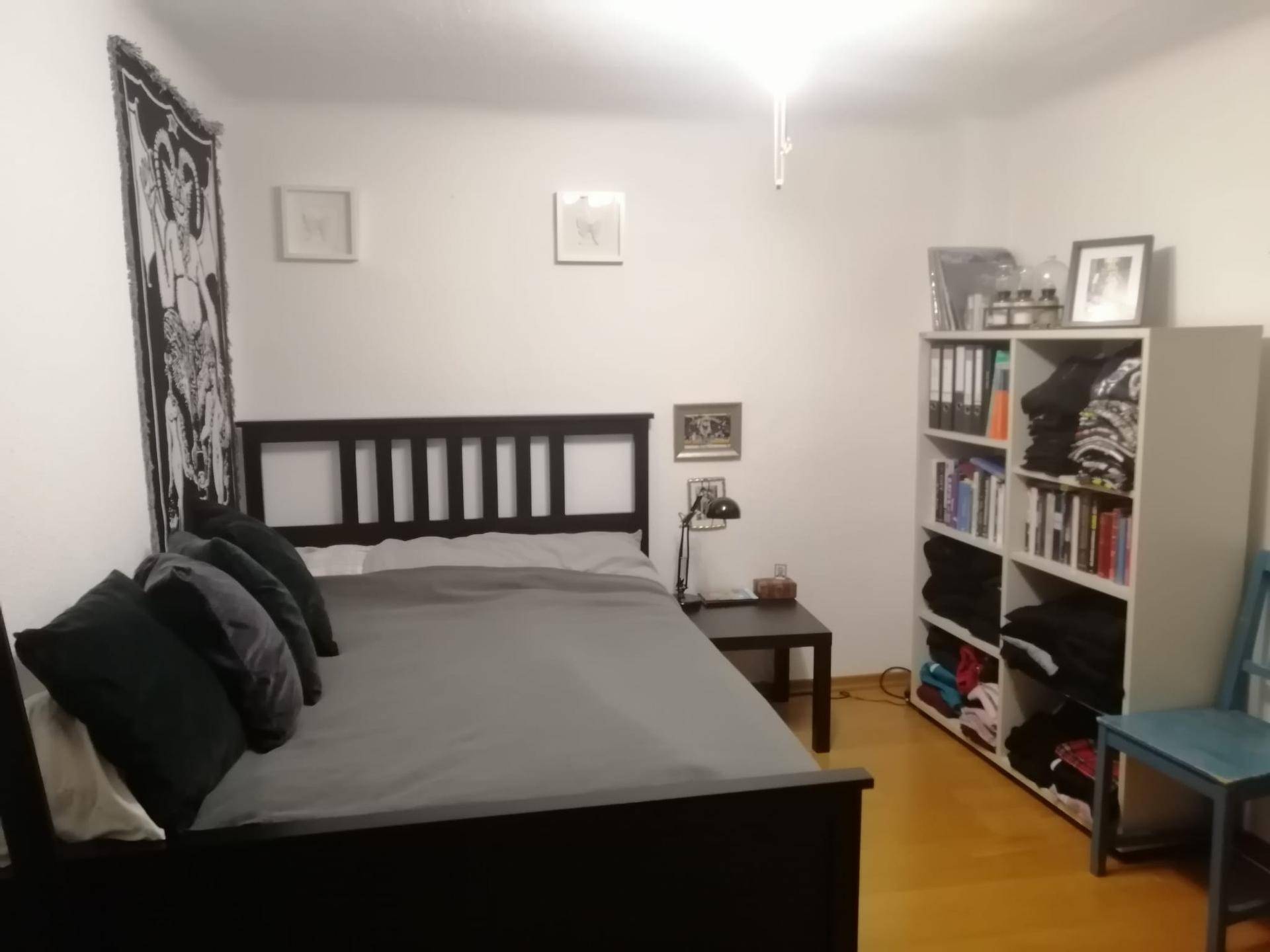Schlafzimmer mit einem Doppelbett, Nachttisch, Leselampe und einem praktischen Bücherregal.