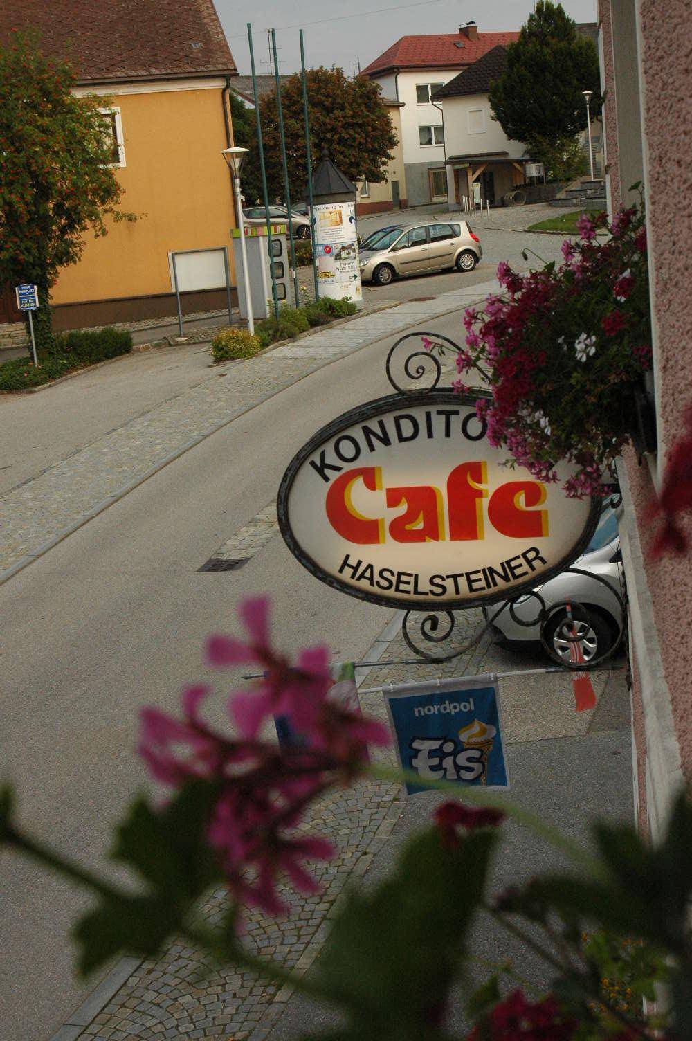 Blick von einem Fensterkasten auf die belebte Straße und das markante Schild der Konditorei Haselsteiner.
