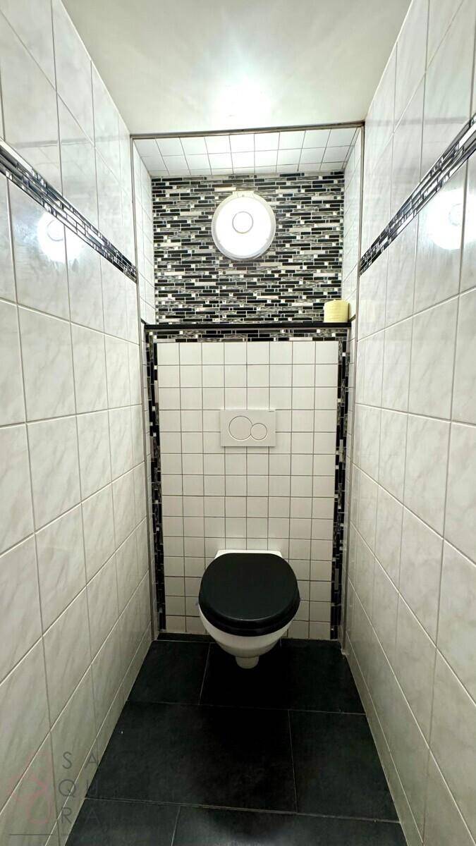 Gäste-WC mit weißen Fliesen, wandhängender Toilette und dekorativer Mosaikwand.