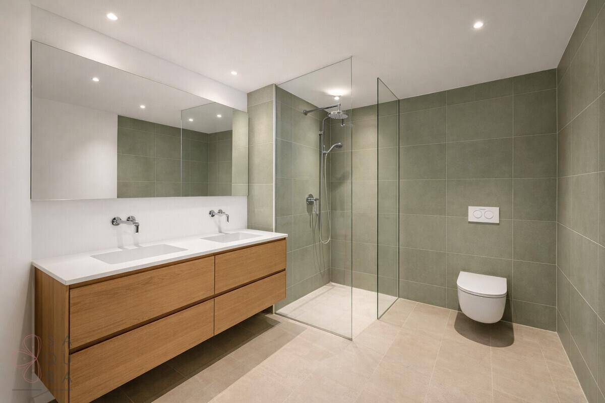 Modernes Badezimmer mit Doppelwaschbecken, großer begehbarer Dusche und hellgrünen Fliesen.