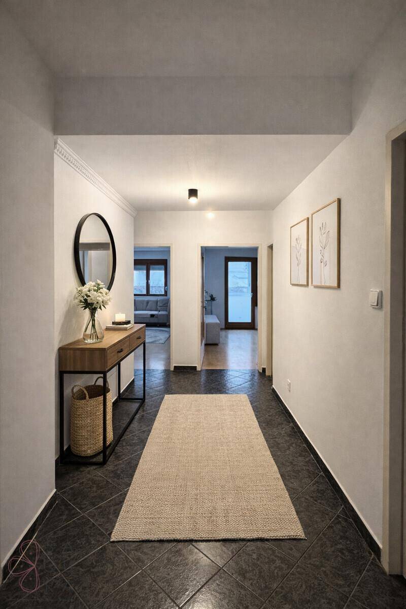 Langer Flur mit dunklem Fliesenboden, dekorativem Spiegel und Blick in angrenzende Räume.