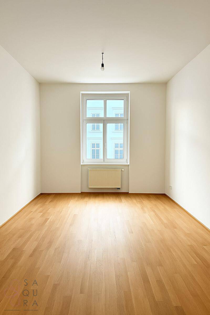 Heller, leerer Raum mit Laminatboden und großem Fenster mit Stadtblick.