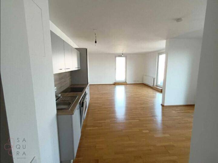 Heller Wohnbereich mit Küchenzeile und Parkettboden, mit Blick auf die großen Fenster.