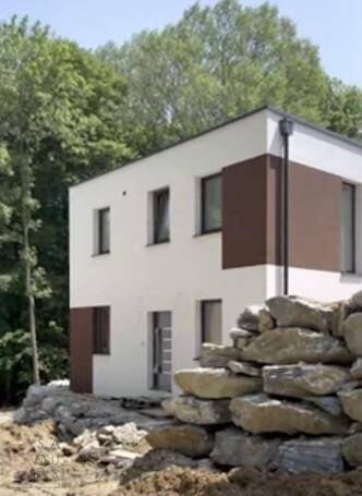 Modernes Haus im Bau mit weißer und brauner Fassade, umgeben von Felsen und Bäumen.