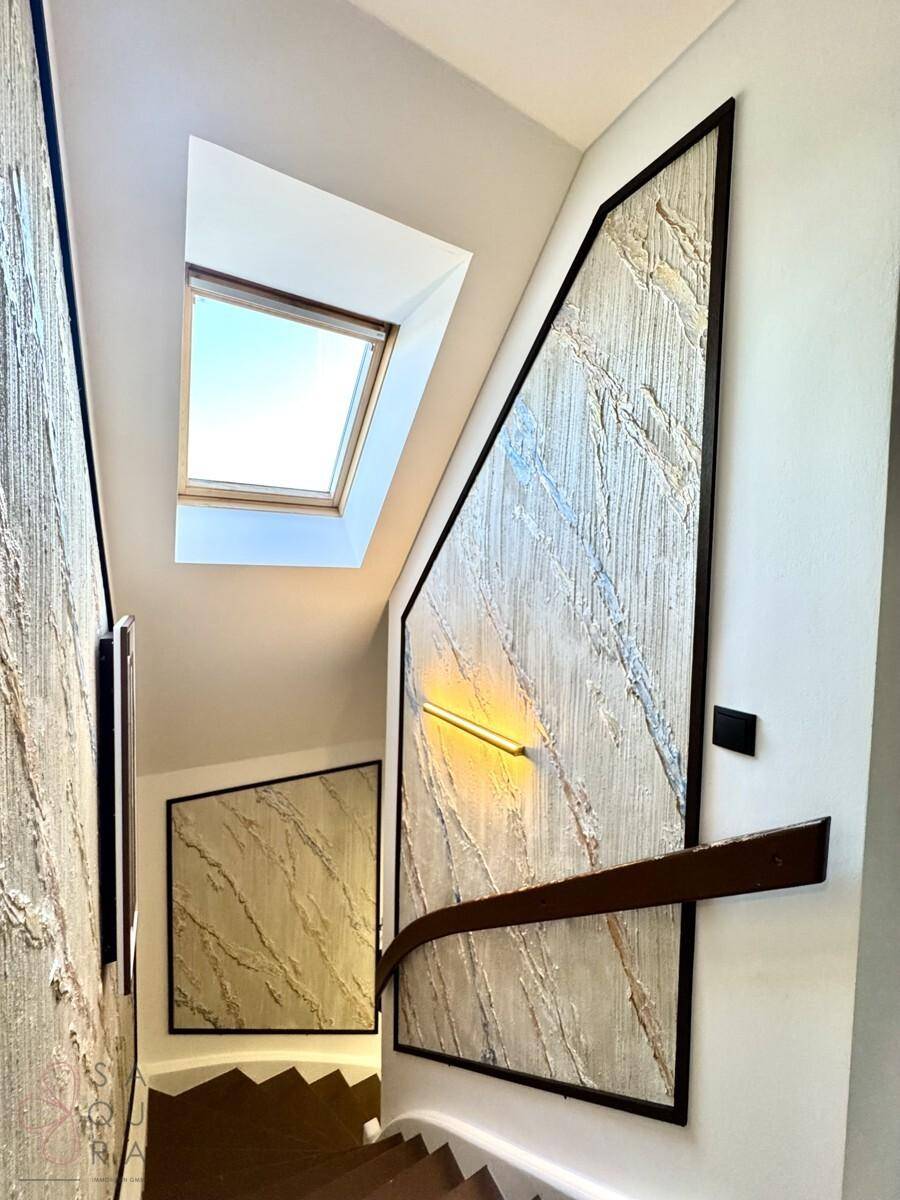 Treppenhaus mit dekorativen Wandpaneelen, Holzgeländer und Dachfenster für natürliches Licht.