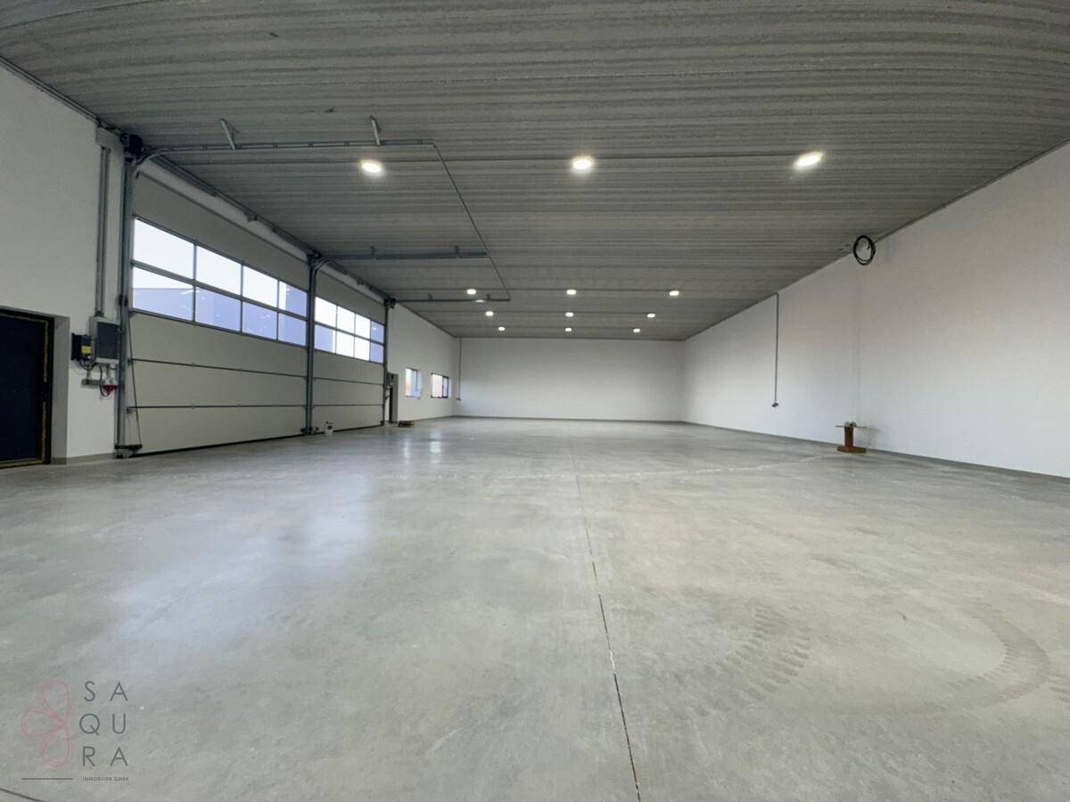 Weitläufige, leere Lagerhalle mit Betonboden, hohen Decken und mehreren Rolltoren.